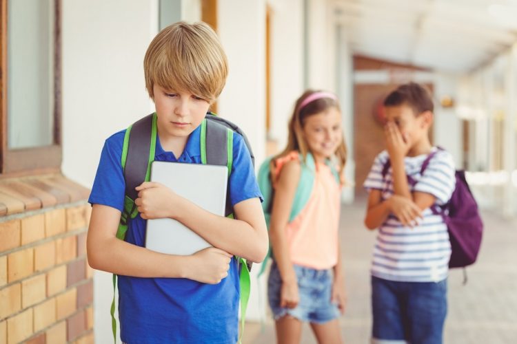 School friends bullying a sad boy in corridor at school